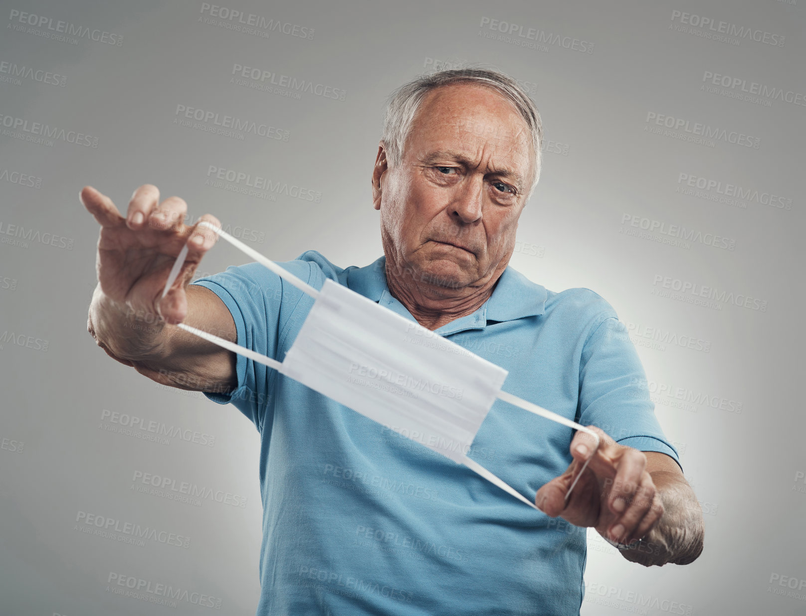 Buy stock photo Shot of an older man looking at a face mask in confusion in a studio against a grey background