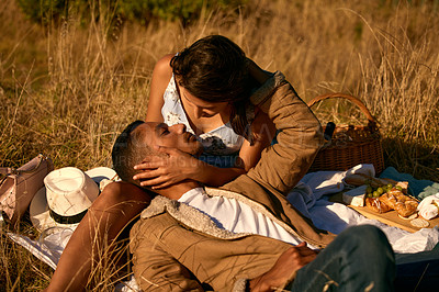 Buy stock photo Love, sunset and picnic with couple in field for summer break, relax and romantic date. Happy, kiss and food with man and woman affectionate in grass of countryside for travel, bonding and peace