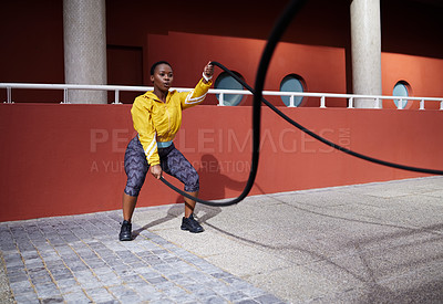 Buy stock photo Shot of a young woman using battle ropes against an urban background