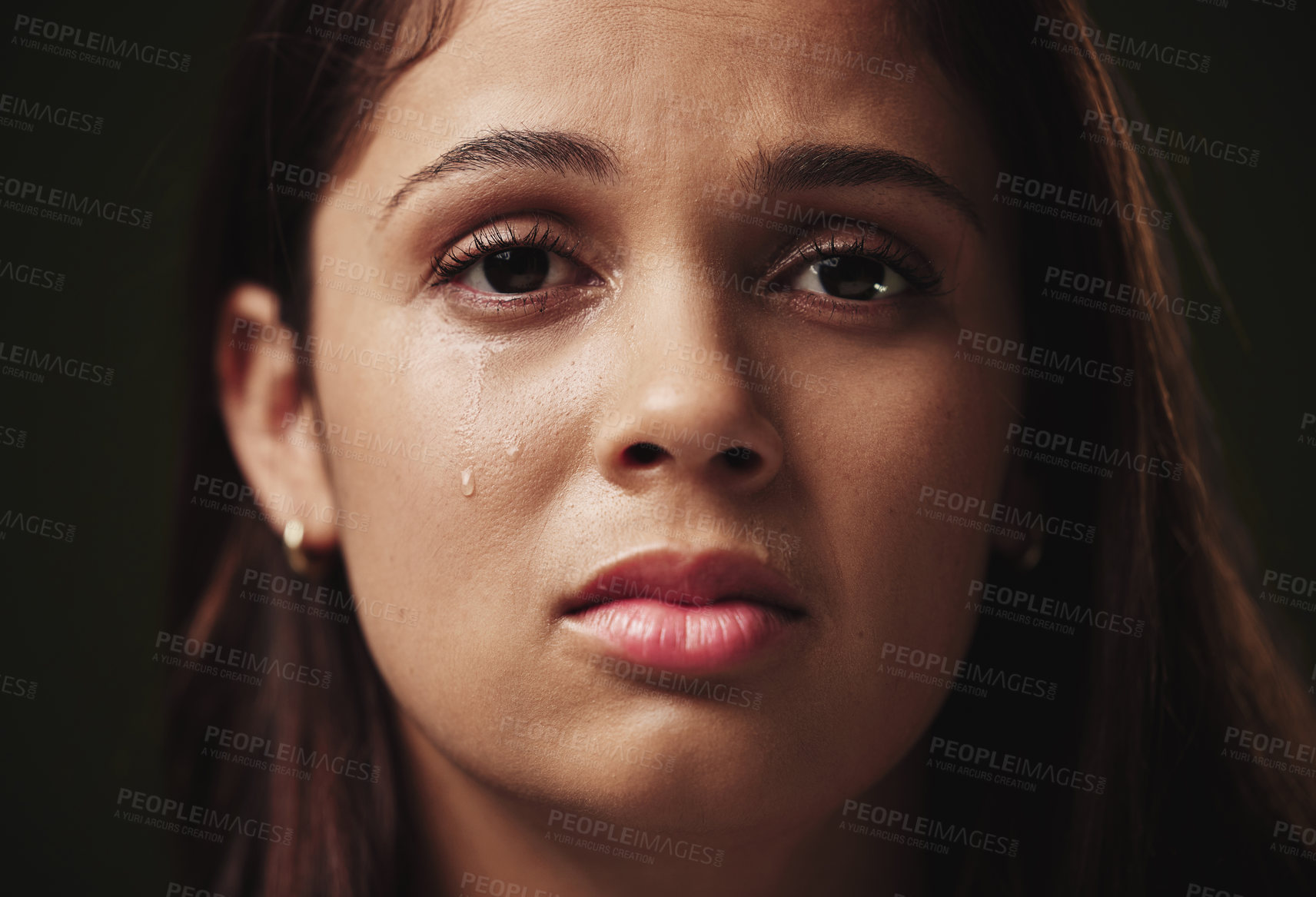 Buy stock photo Cropped portrait of an attractive young woman crying against a dark background