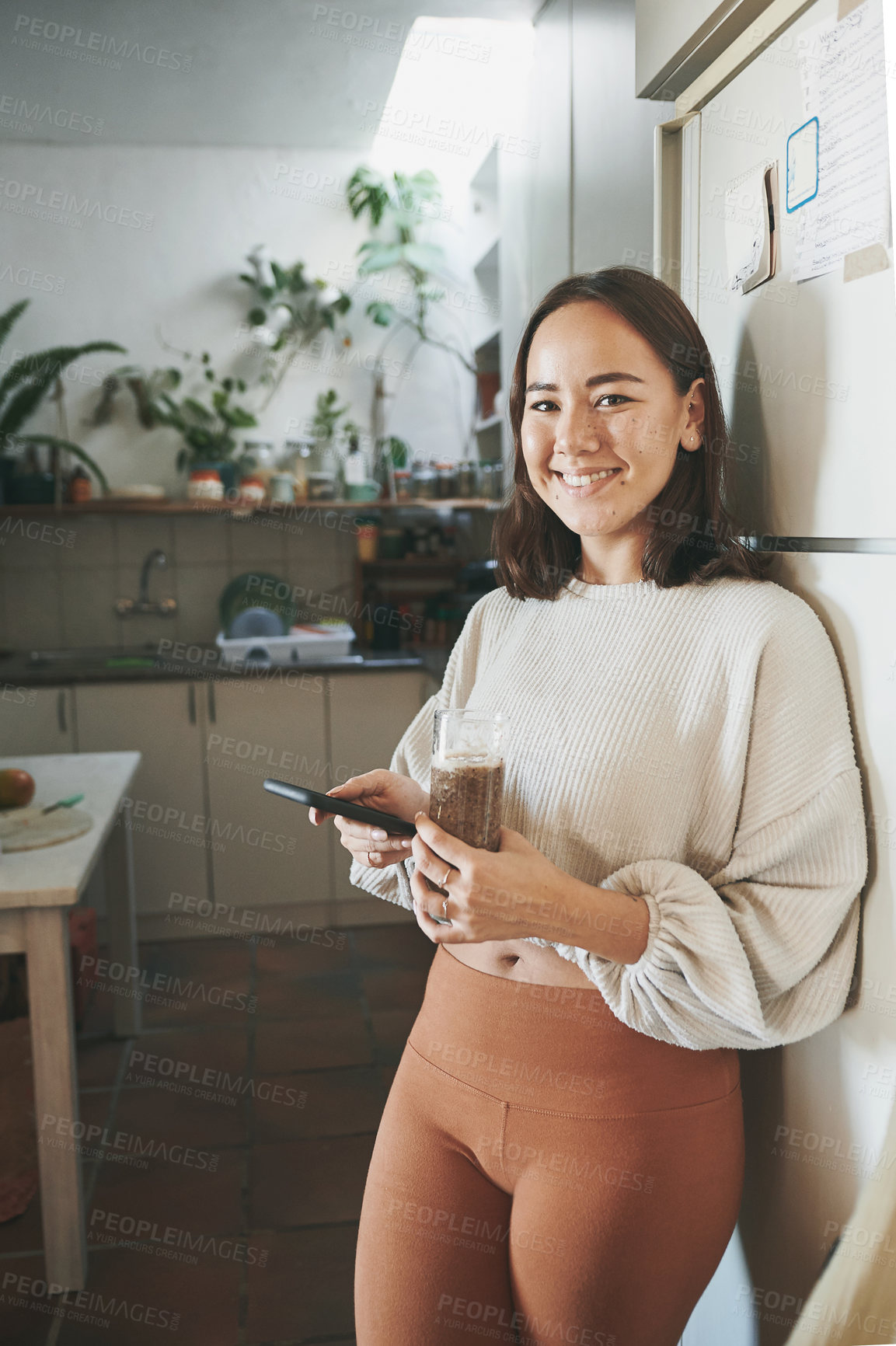 Buy stock photo Shot of a young woman using her smartphone while drinking a smoothie