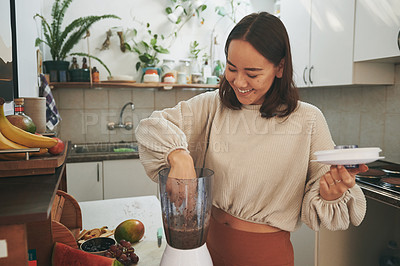Buy stock photo Shot of a young woman dipping her finger into the blender to taste her smoothie