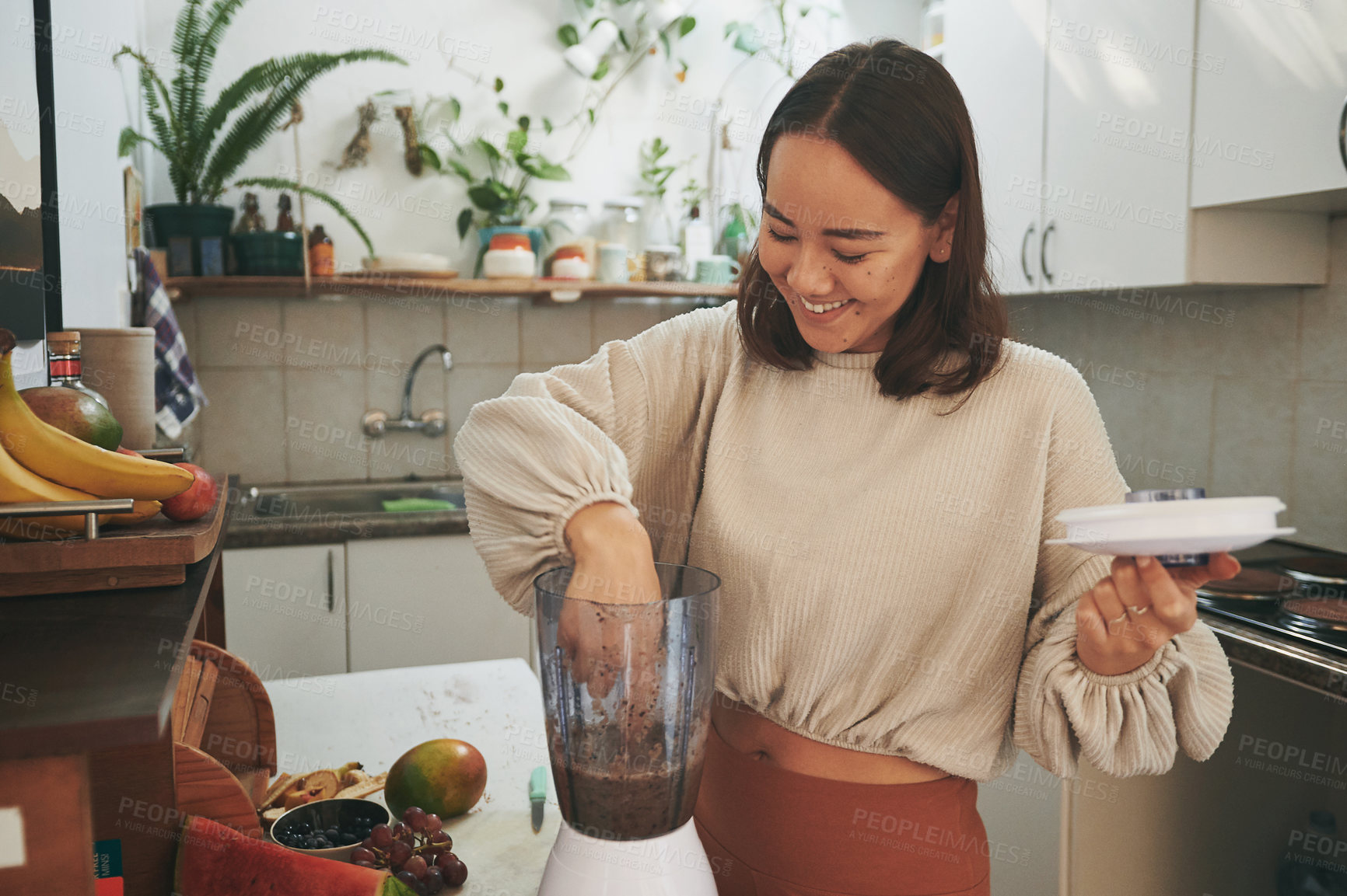 Buy stock photo Shot of a young woman dipping her finger into the blender to taste her smoothie
