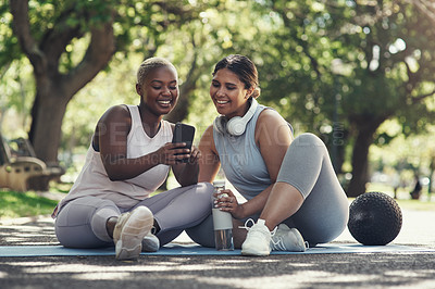 Buy stock photo Shot of two female friends taking a break to use a smartphone while working out
