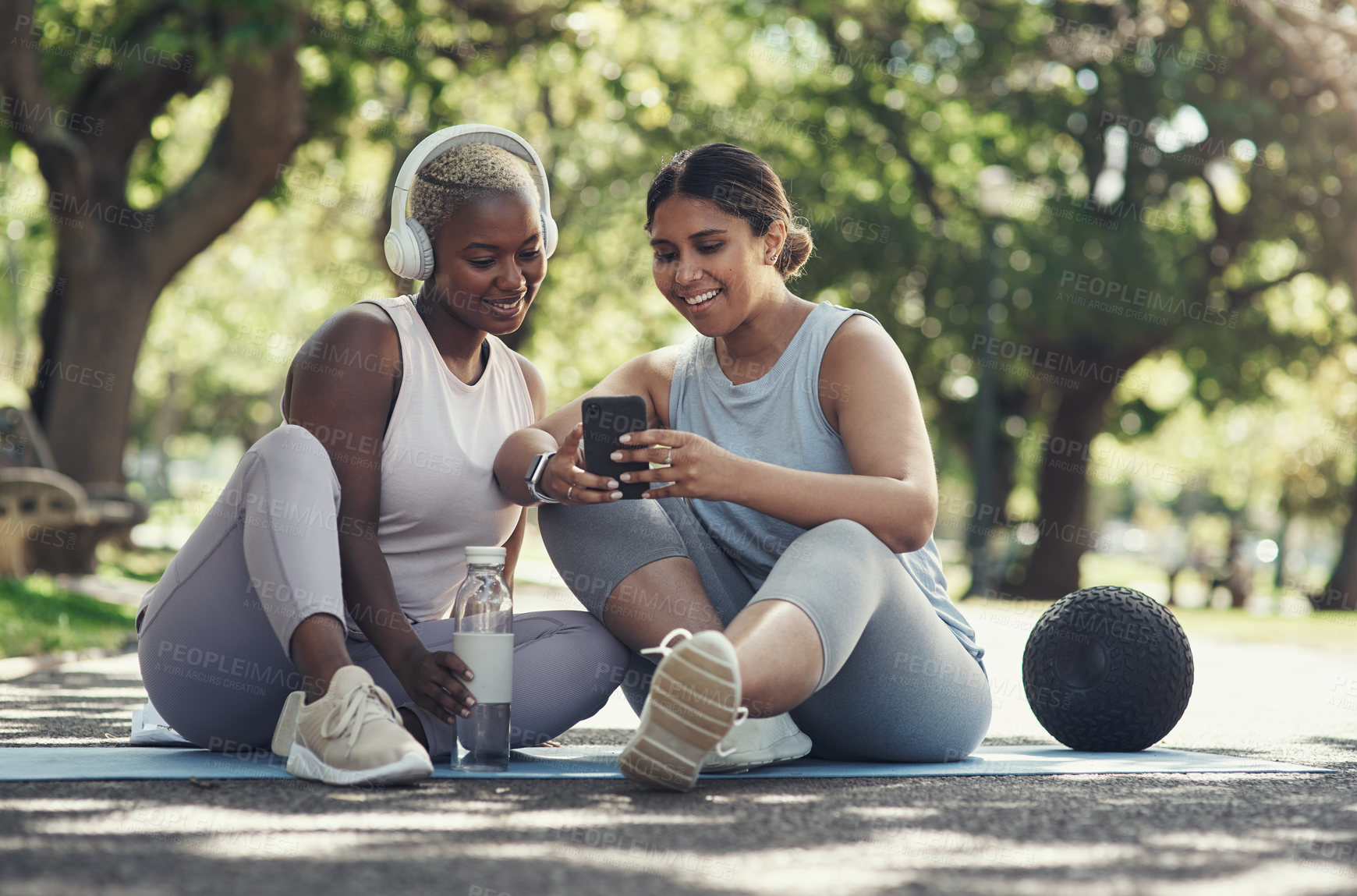 Buy stock photo Shot of two female friends taking a break to use a smartphone while working out