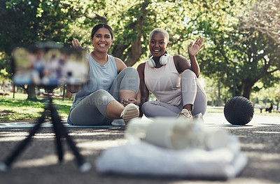 Buy stock photo Shot of two female friends taking a break to livestream their workout