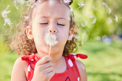 Buy stock photo Shot of an adorable little girl blowing a dandelion while sitting at the park