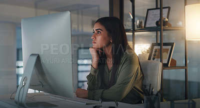 Buy stock photo Shot of a young businesswoman looking thoughtful while working on a computer in an office at night