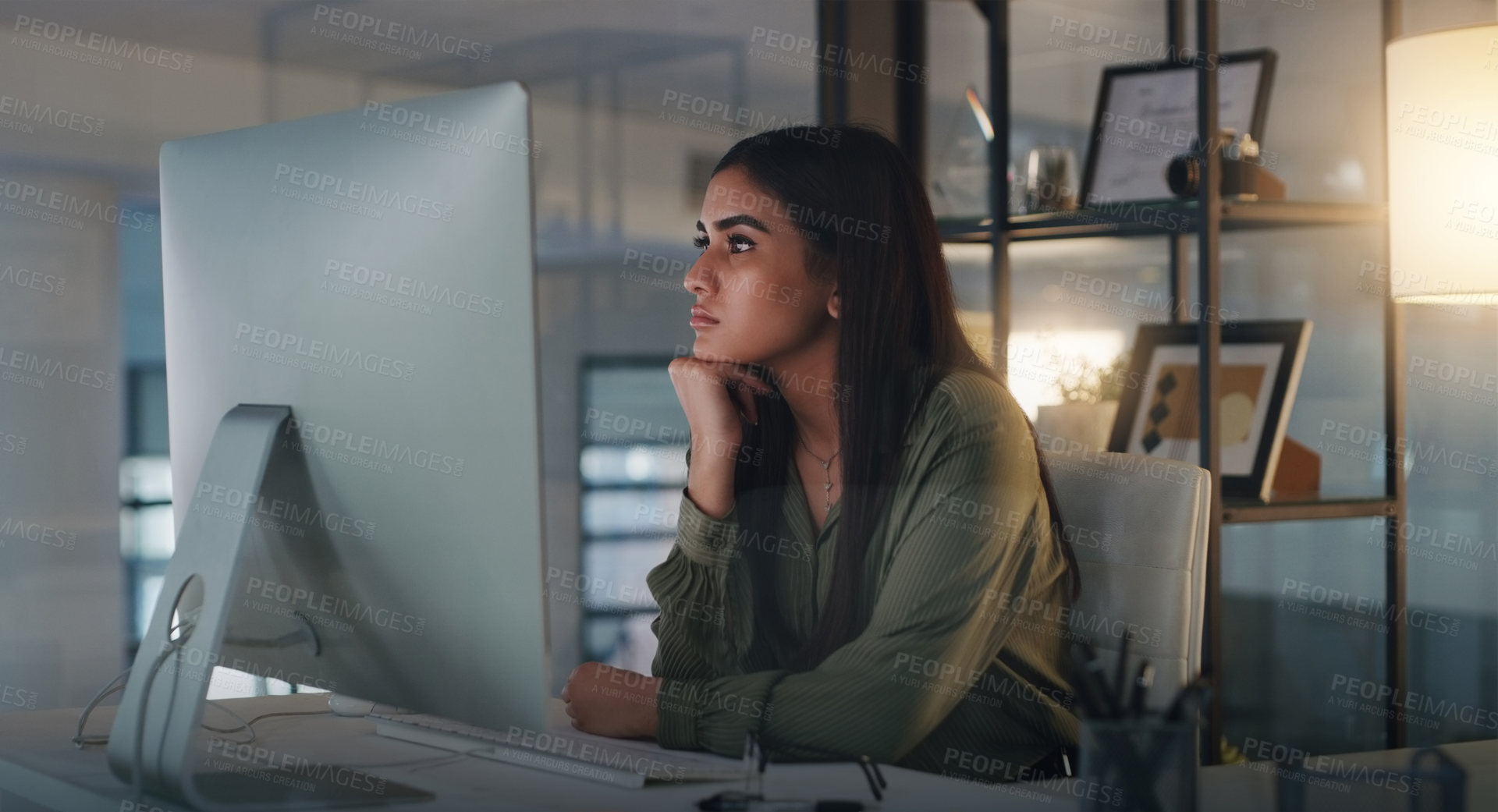 Buy stock photo Shot of a young businesswoman looking thoughtful while working on a computer in an office at night