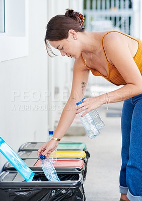 Buy stock photo Shot of an attractive young woman standing down and putting plastic bottles in her recycling bin
