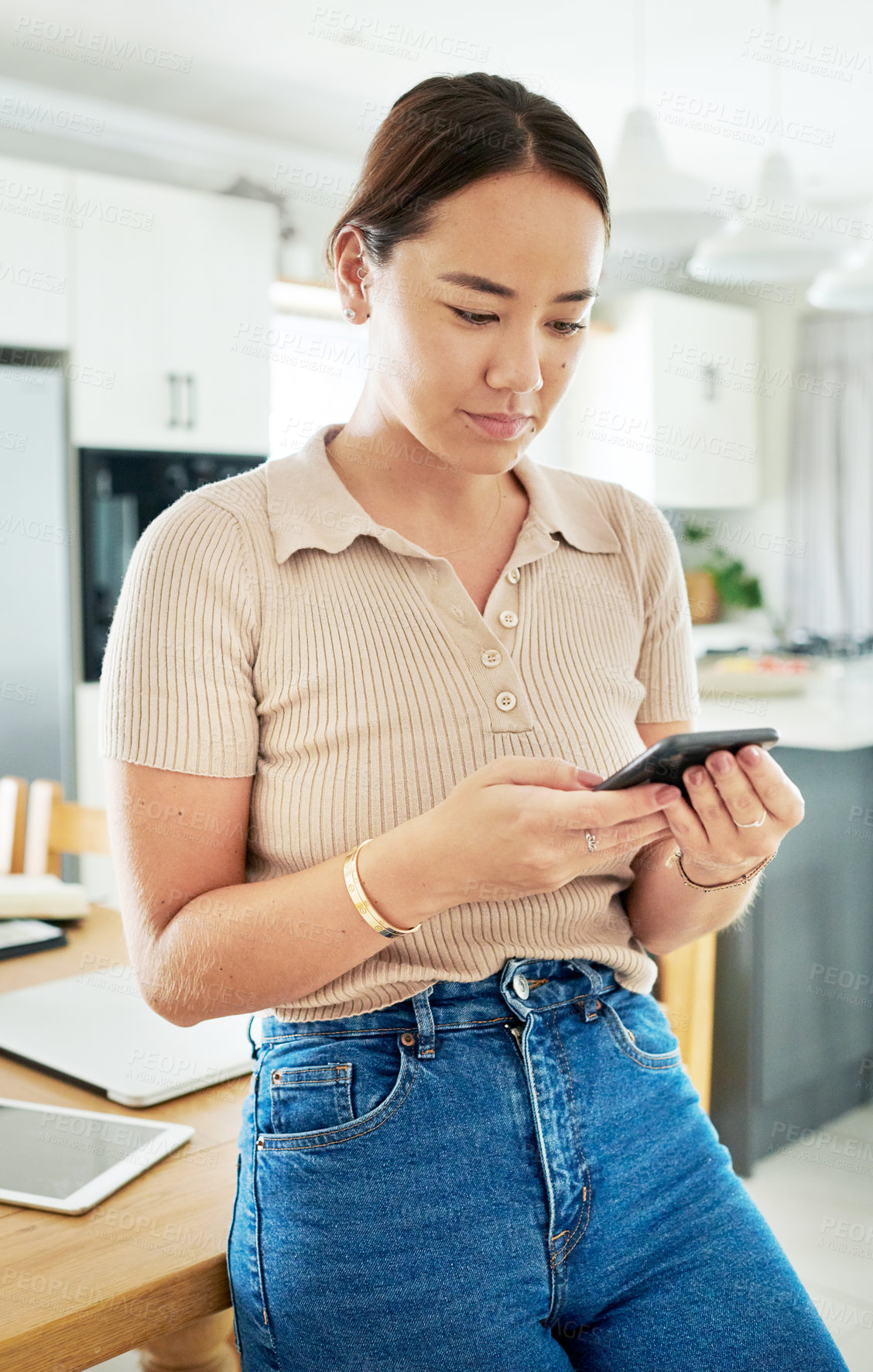 Buy stock photo Phone, reading and woman in kitchen networking on mobile app, internet or website at home. Technology, communication and young Asian female person scroll on cellphone by table at modern apartment.