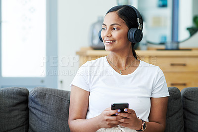 Buy stock photo Home, smartphone and woman with headphones, relax and smile with live streaming and sound. Apartment, girl on couch and person with headset, thinking and cellphone with audio and listening to podcast
