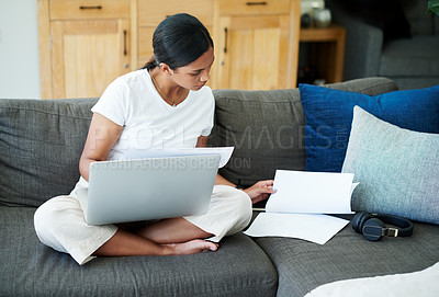 Buy stock photo Shot of an attractive young woman sitting on her sofa at home and calculating her finances on her laptop