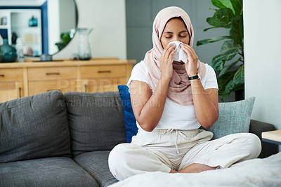 Buy stock photo Muslim, woman and sick or sneezing on sofa in living room with illness, flu and tired at home. Female person, lounge and couch for cold, fever and virus with blowing nose on recovery or rest