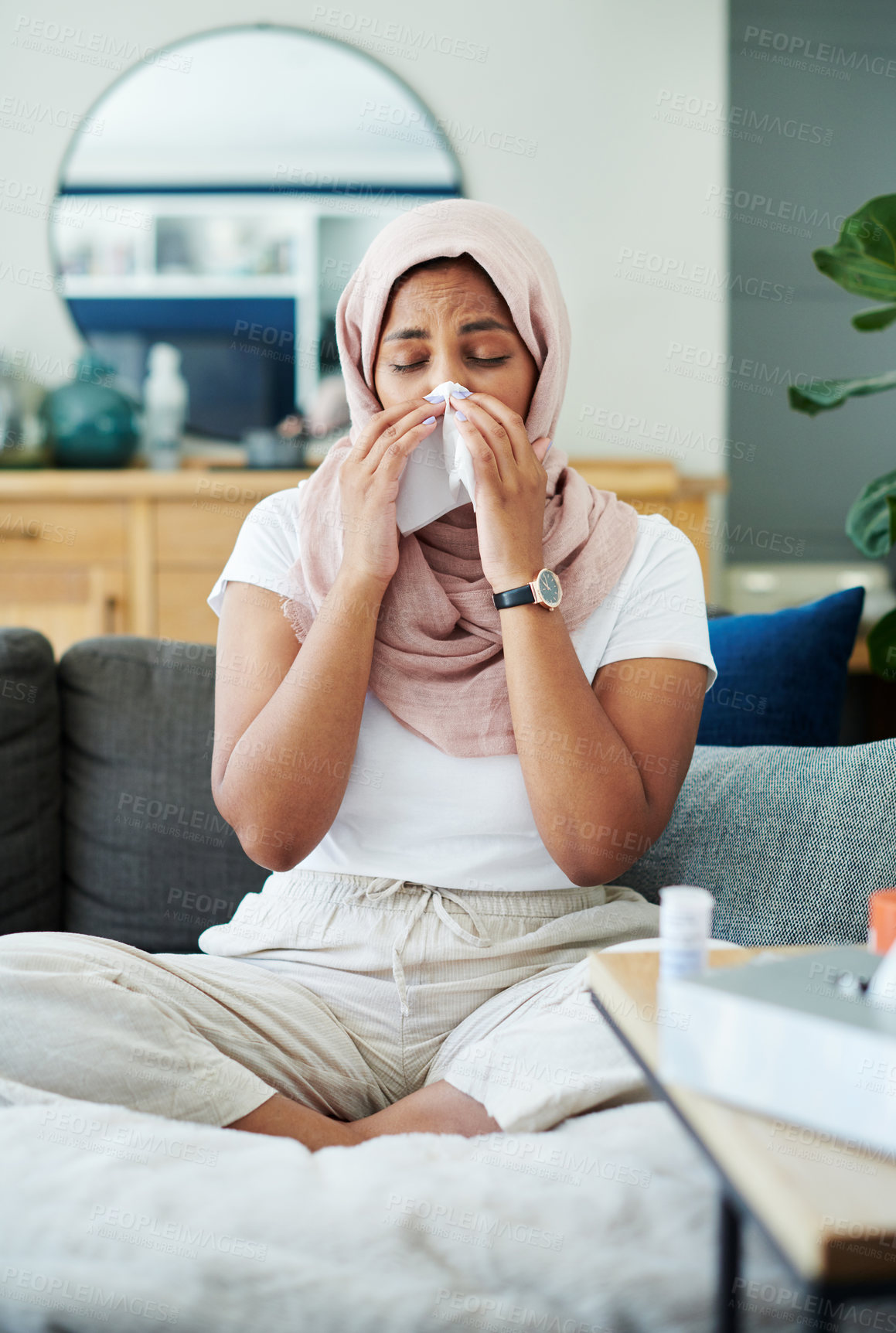 Buy stock photo Muslim, woman and sick or sneezing on couch in living room with illness, flu and tired at home. Female person, lounge and fever with medication to relax, chill and calm on sofa for recovery or rest
