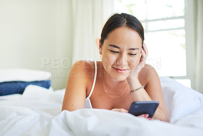 Buy stock photo Shot of an attractive young woman lying on her bed and using her cellphone in the morning