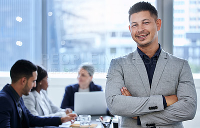 Buy stock photo Portrait of a confident young businessman standing in an office with his colleagues in the background