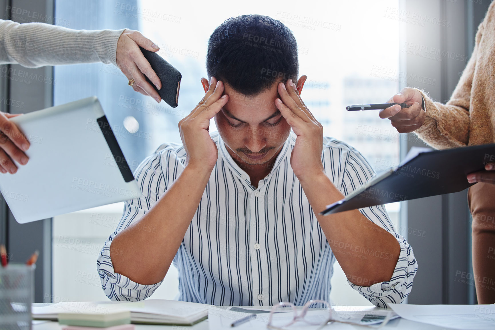 Buy stock photo Shot of a young businessman sitting in the office and feeling stressed while colleagues overwhelm him with tasks