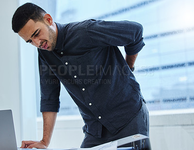 Buy stock photo Shot of a young businessman standing alone in the office and suffering from backache