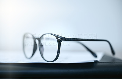 Buy stock photo Shot of a pair of glasses lying on a desk in an empty office during the day