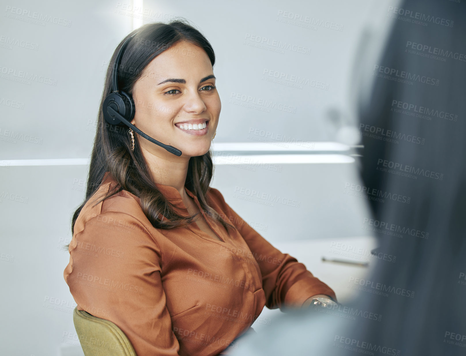 Buy stock photo Shot of an attractive young saleswoman sitting in the office with a colleague and wearing a headset