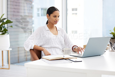 Buy stock photo Shot of a young businesswoman sitting at a desk using a laptop in a modern office