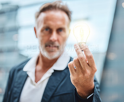 Buy stock photo Shot of a mature businessman holding a lightbulb against an urban background