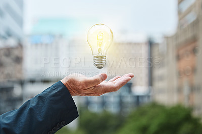 Buy stock photo Shot of an unrecognisable businessman holding a lightbulb against an urban background