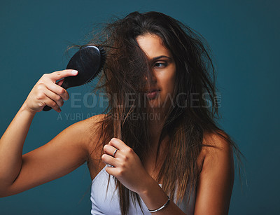Buy stock photo Studio shot of a beautiful young woman holding a brush to her hair posing against a blue background