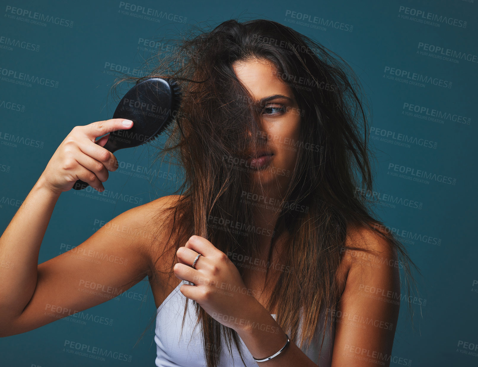 Buy stock photo Studio shot of a beautiful young woman holding a brush to her hair posing against a blue background