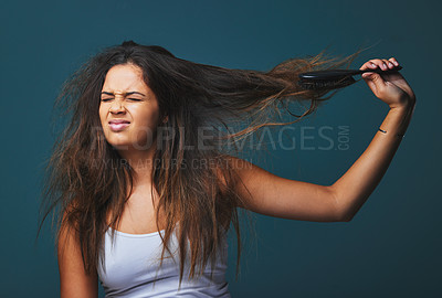 Buy stock photo Studio shot of a beautiful young woman pulling on her hair posing against a blue background