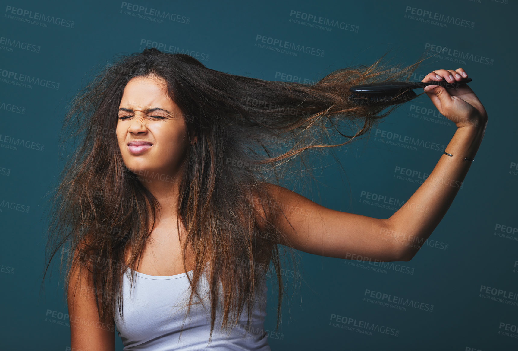 Buy stock photo Studio shot of a beautiful young woman pulling on her hair posing against a blue background