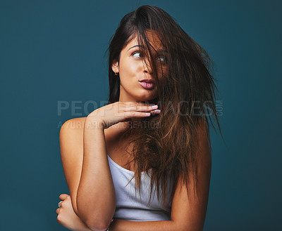 Buy stock photo Studio shot of a beautiful young woman holding her hand to her face posing against a blue background