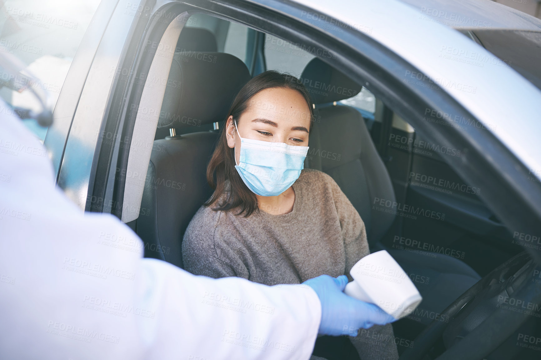 Buy stock photo Shot of a masked young woman getting her temperature checked by a doctor while sitting in her car