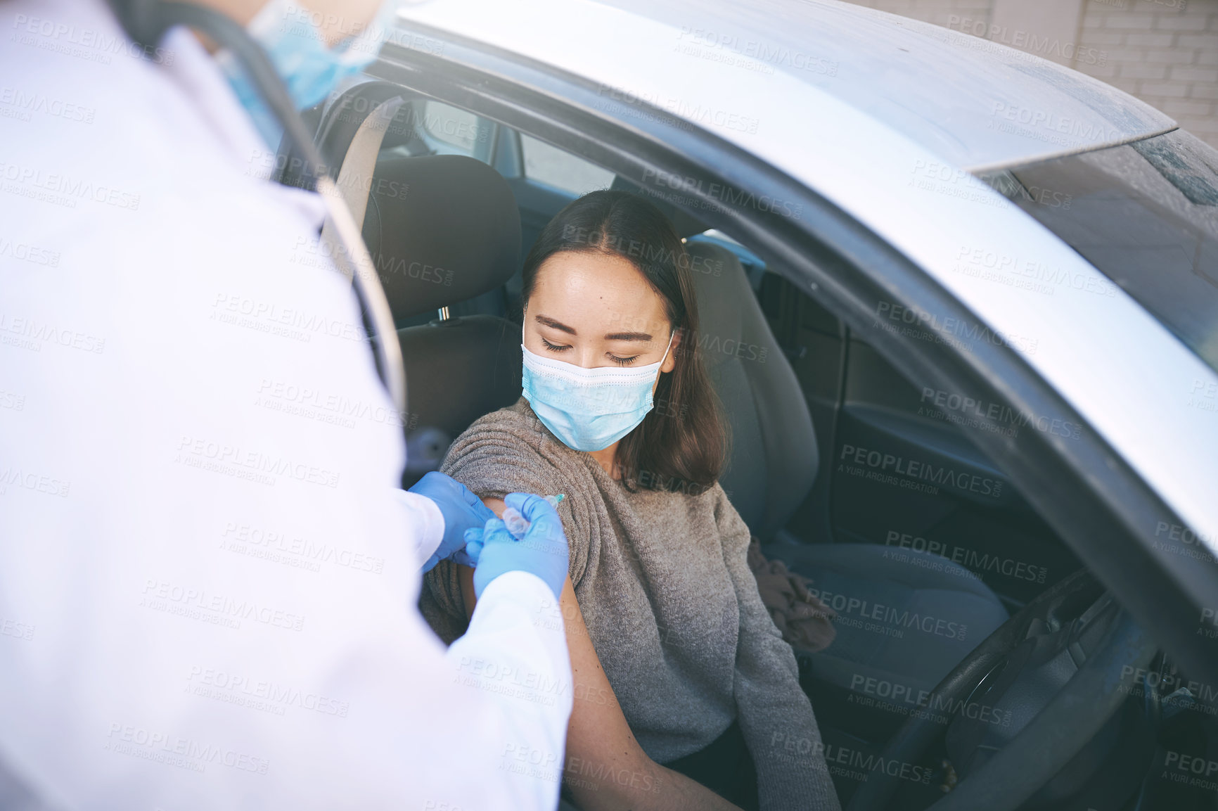 Buy stock photo Shot of a masked young woman receiving an injection at a Covid-19 drive through testing centre