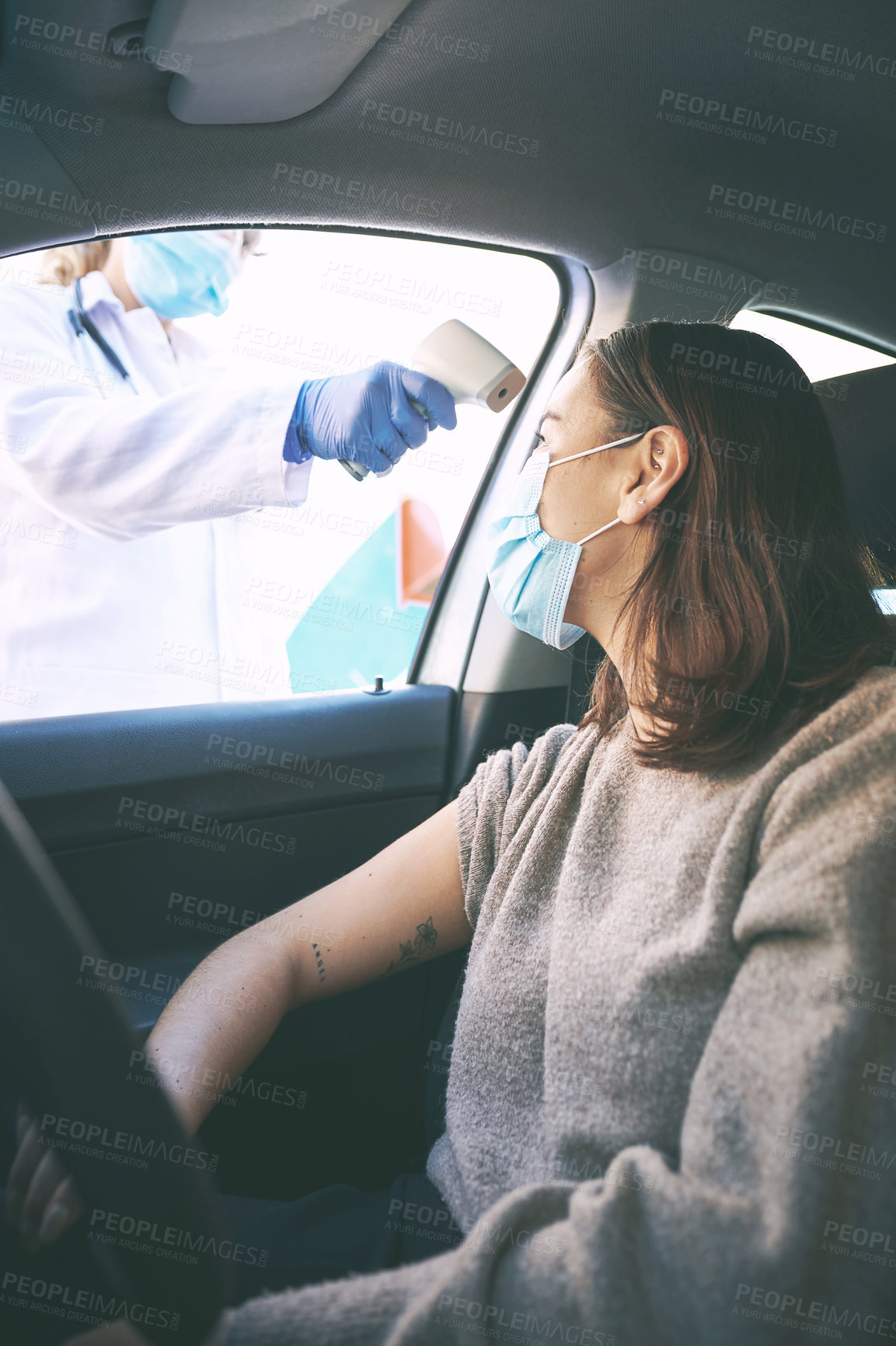 Buy stock photo Shot of a masked young woman getting her temperature checked by a doctor while sitting in her car