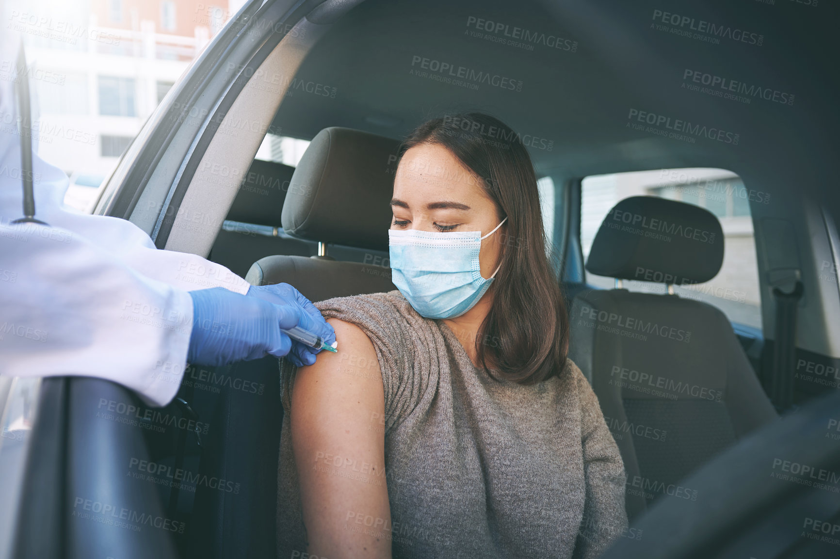 Buy stock photo Shot of a masked young woman receiving an injection at a Covid-19 drive through testing centre