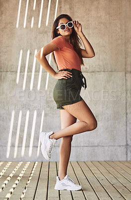 Buy stock photo Shot of an attractive young woman wearing sunglasses posing against an urban background