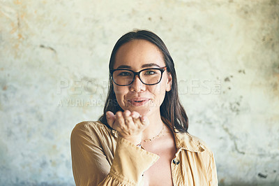 Buy stock photo Portrait of a young woman blowing a kiss while standing against a wall