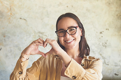 Buy stock photo Portrait of a young woman making a heart shape with her hands against a wall