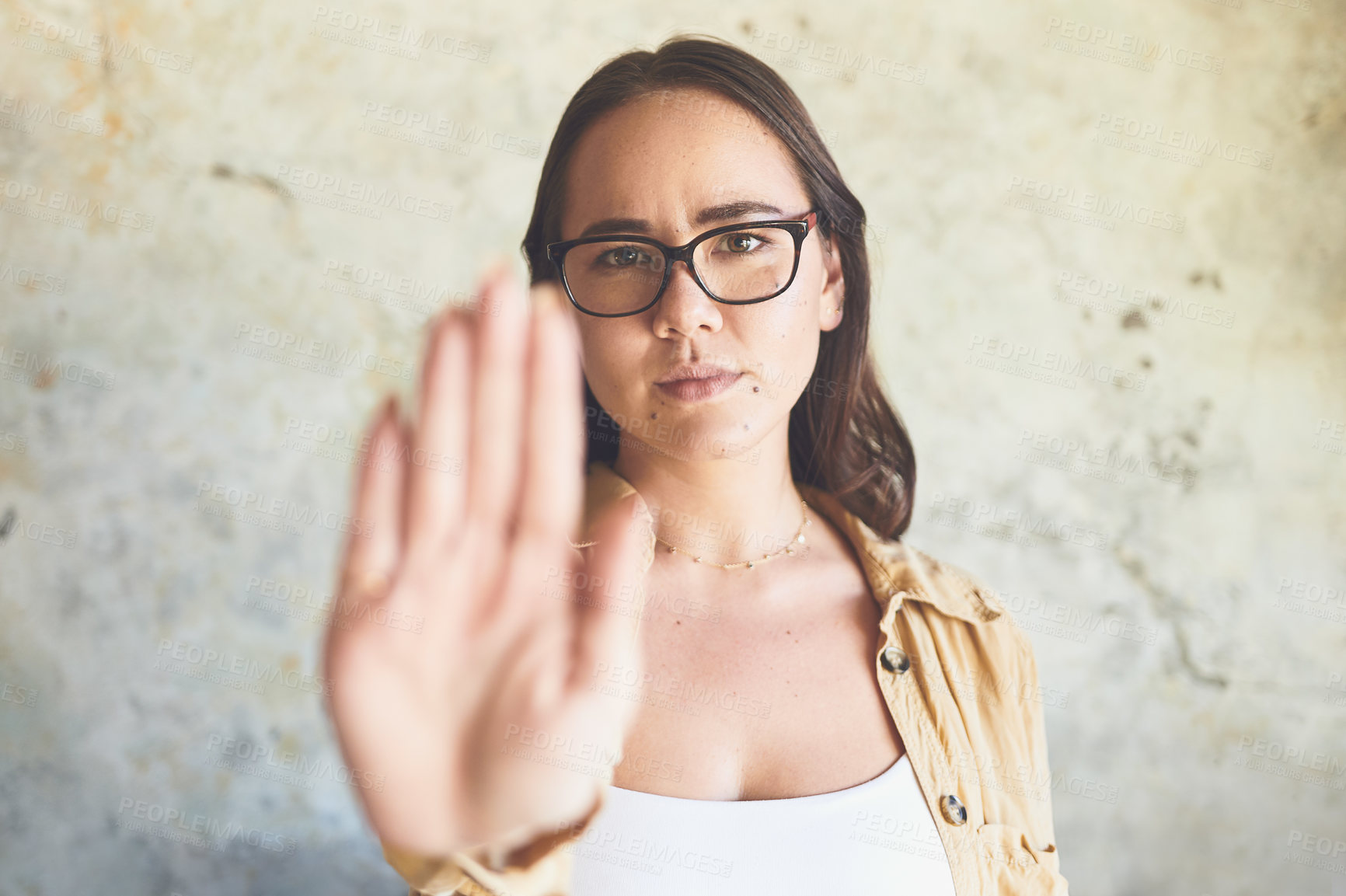 Buy stock photo Portrait of a woman holding up her hand while standing against a wall