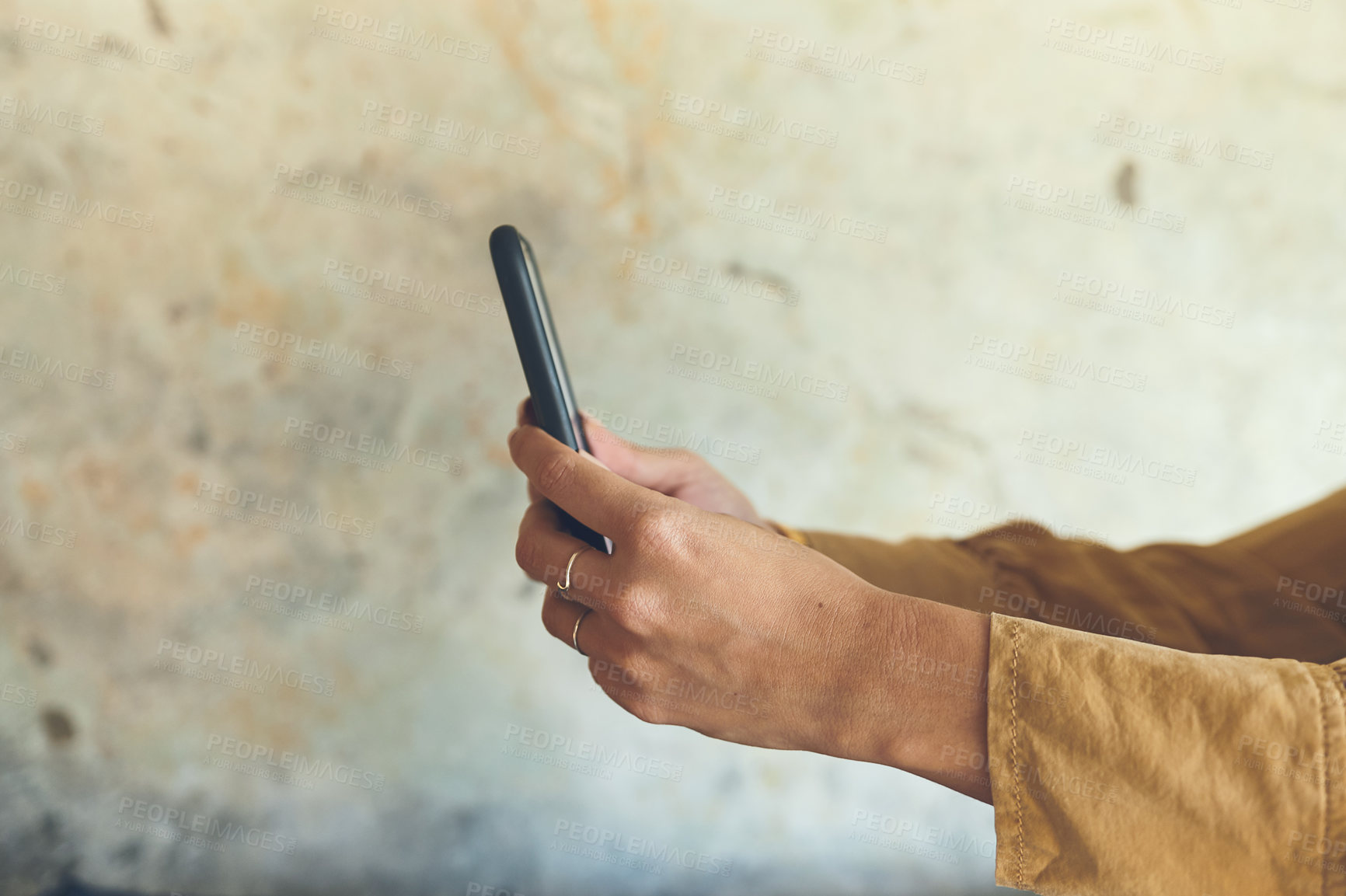 Buy stock photo Closeup shot of an unrecognisable woman using a cellphone against a wall