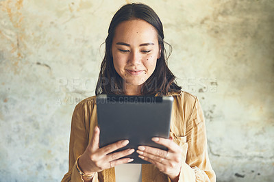 Buy stock photo Shot of a young woman using a digital tablet while standing against a wall