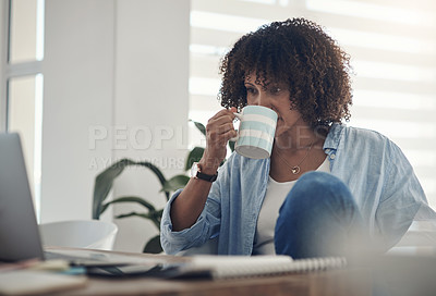 Buy stock photo Shot of an attractive young woman sitting alone at home and using her laptop while drinking a cup of coffee