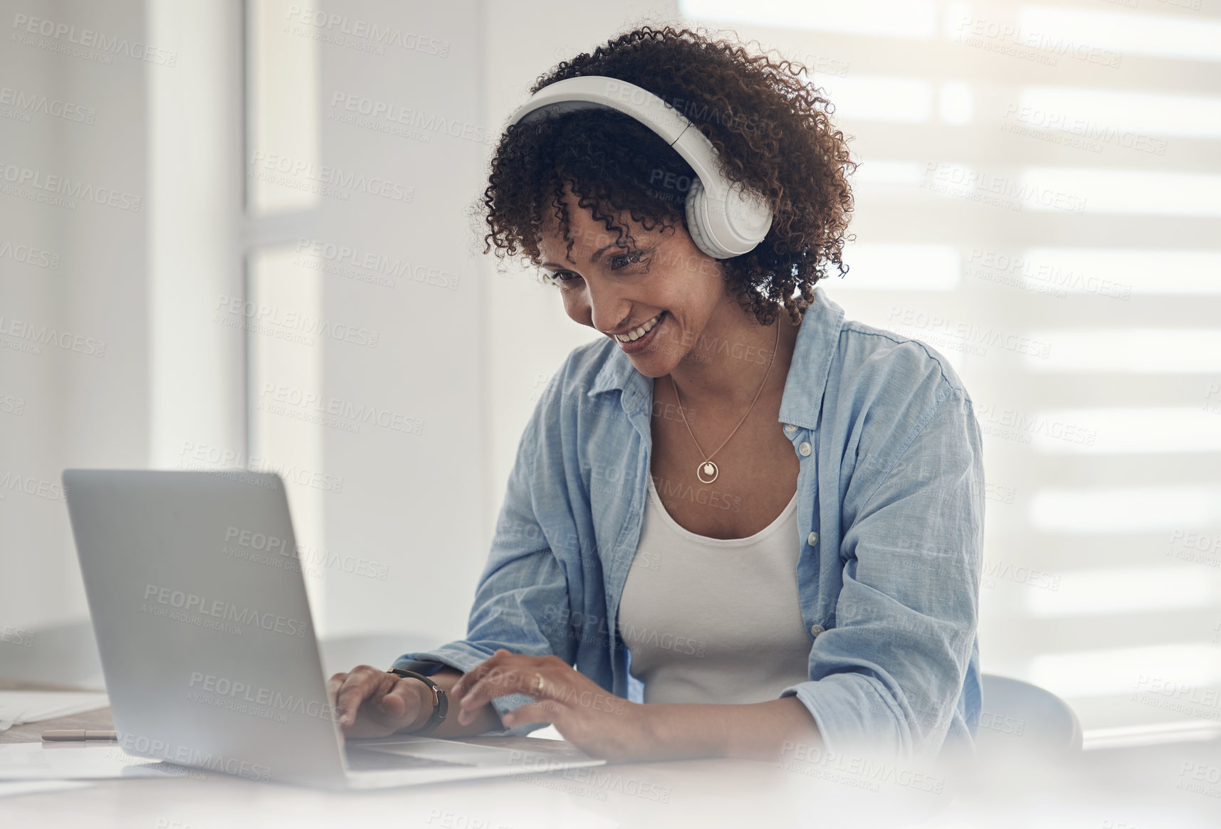 Buy stock photo Shot of an attractive young woman sitting alone at home and using her laptop while wearing headphones