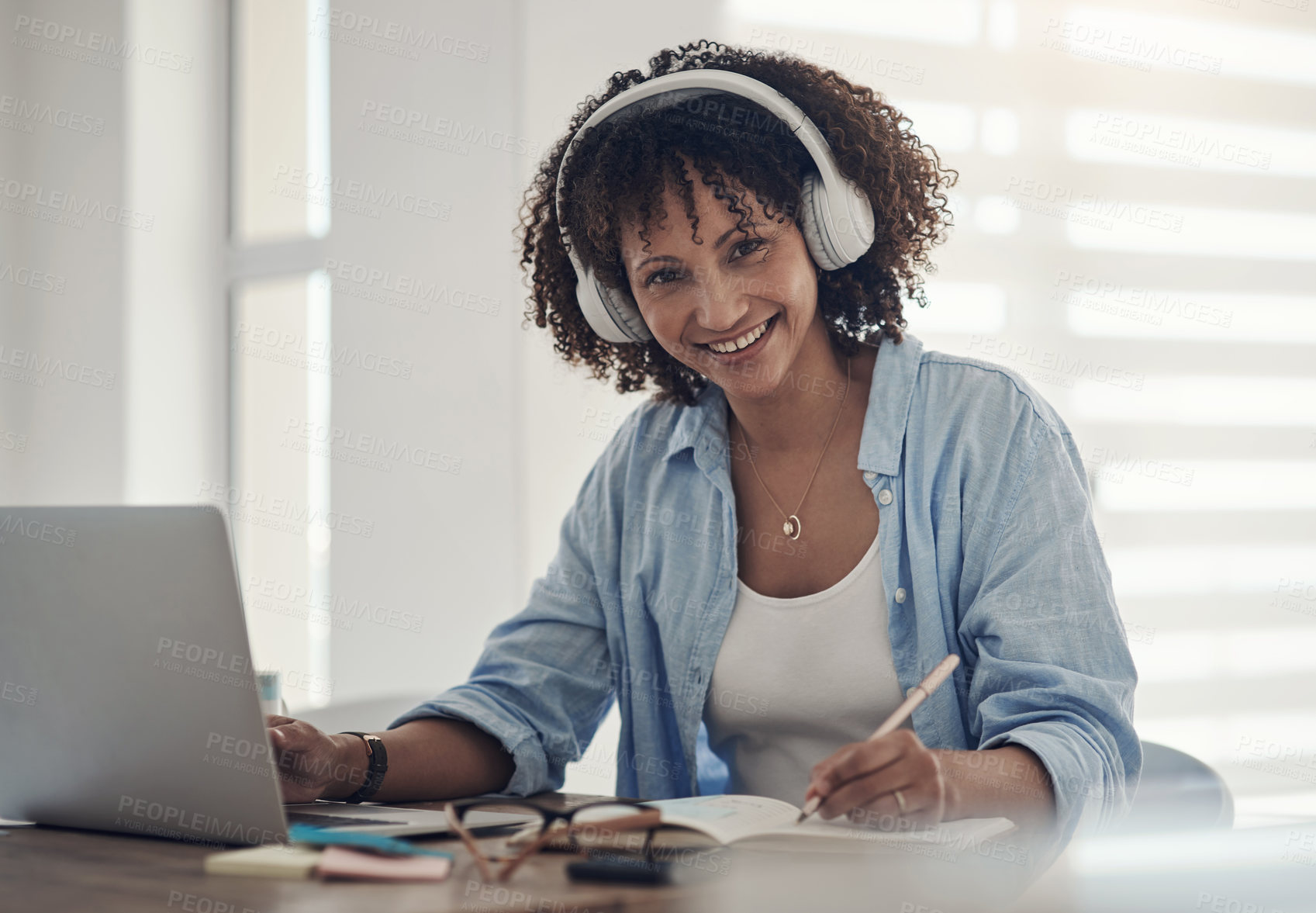 Buy stock photo Shot of an attractive young woman sitting alone in her home and writing in a notebook while wearing headphones