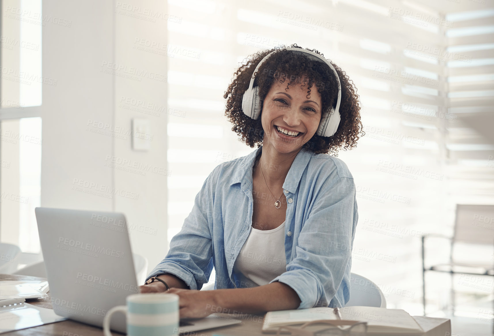 Buy stock photo Shot of an attractive young woman sitting alone at home and using her laptop while wearing headphones