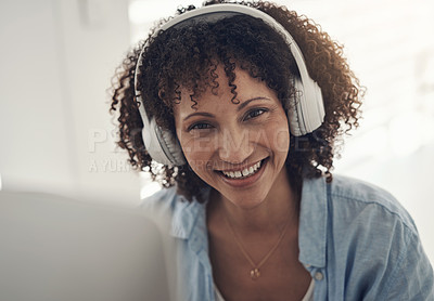 Buy stock photo Shot of an attractive young woman sitting alone at home and using her laptop while wearing headphones