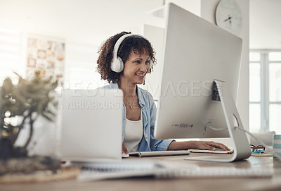 Buy stock photo Shot of an attractive young woman sitting alone at home and using her computer while wearing headphones