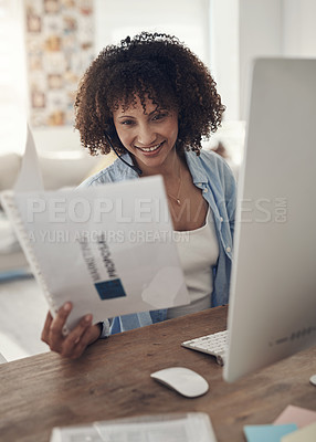 Buy stock photo Shot of an attractive young woman sitting alone at home and using her computer while reading paperwork